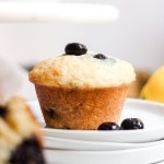 A lemon blueberry muffin on a white plate with fresh blueberries.