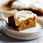 A slice of pumpkin cake with cream cheese icing onto a stack of small white plates.