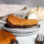 A slice of pumpkin pie with gingersnap crust on a stack of grey plates.