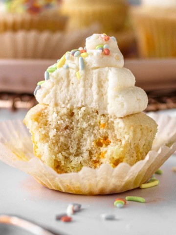 A vanilla cupcake with sprinkles and frosting.