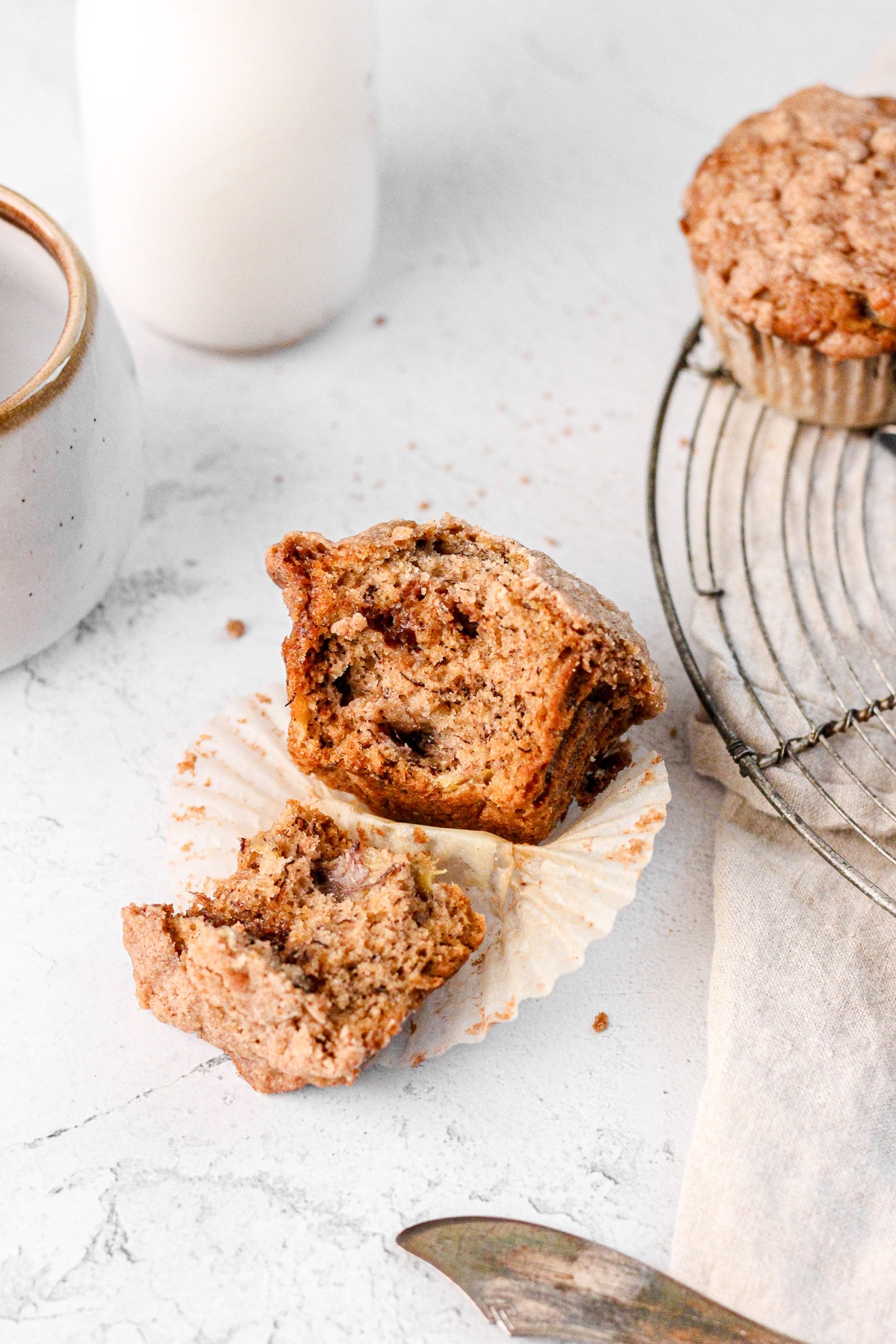 a banana muffin cut in half with a milk jug and wire cooling rack for food photography