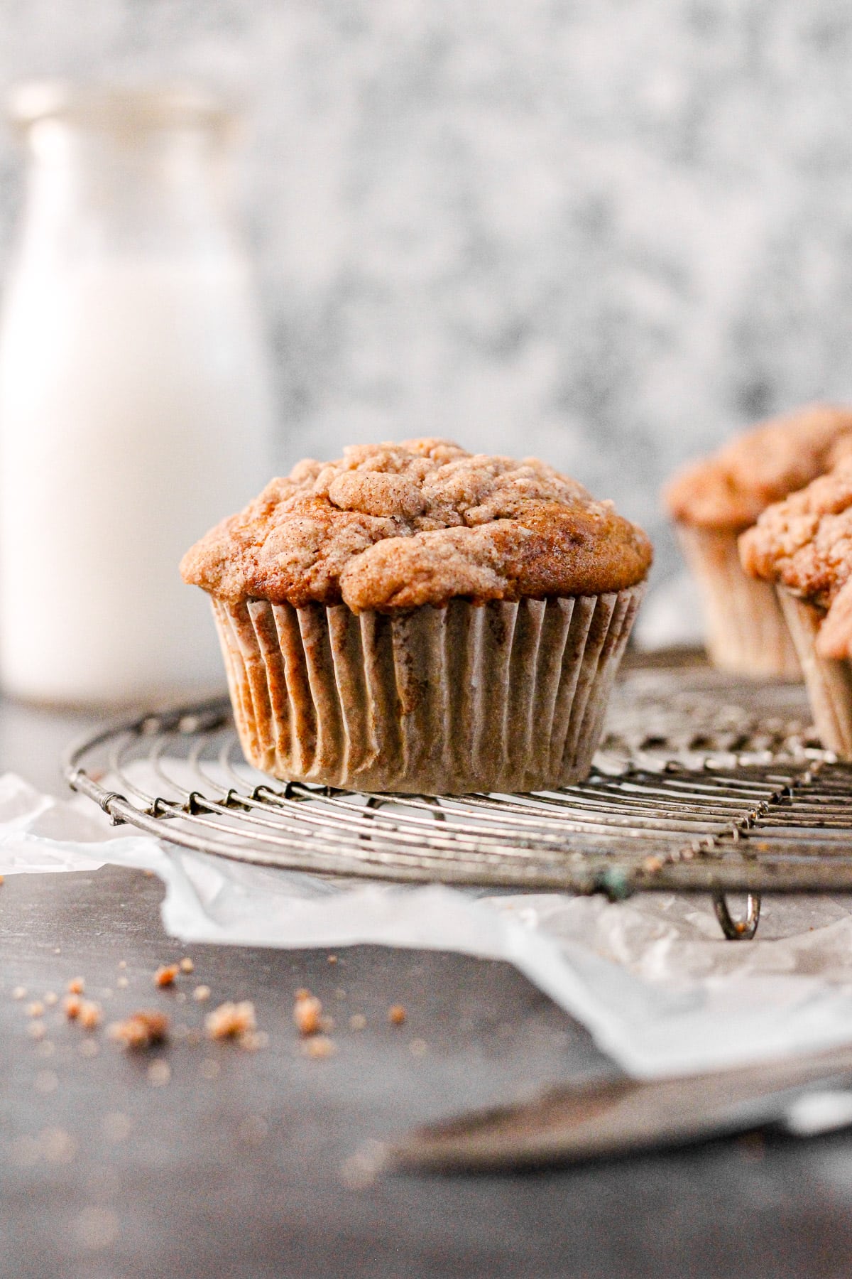 cinnamon banana muffin with streusel topping on a cooling rack with a milk jug for baking blog