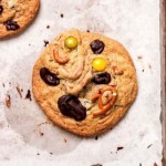 A kitchen sink cookie with m&ms, pretzels and chocolate on parchment paper.
