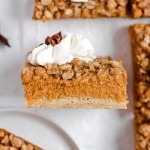 A pumpkin pie bar with streusel topping and whipped cream.