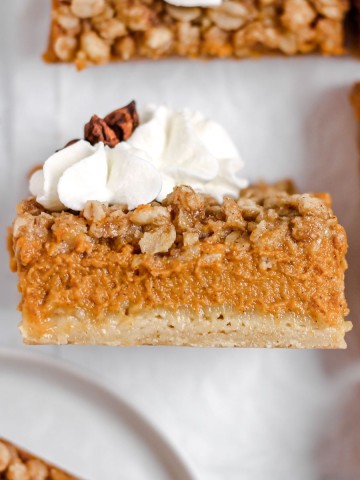 A pumpkin pie bar with streusel topping and whipped cream.