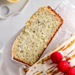A slice of lemon poppy seed loaf cake with fresh raspberries and a simple glaze.