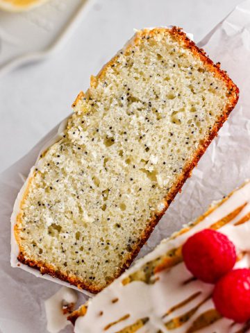 A slice of lemon poppy seed loaf cake with fresh raspberries and a simple glaze.