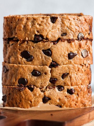 Slices of chocolate chip banana bread stacked on a wooden cutting board.