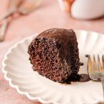 A slice of chocolate cake with chocolate glaze on a plate with a fork.