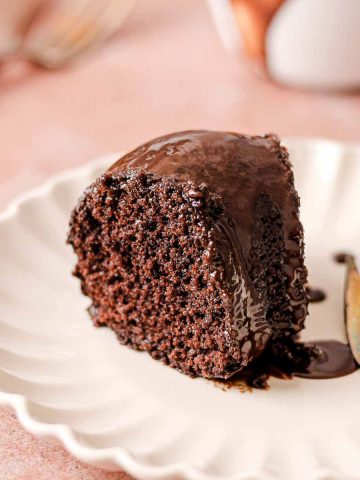 A slice of chocolate cake with chocolate glaze on a plate with a fork.