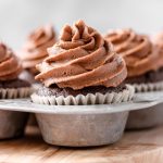 A chocolate cupcake with chocolate buttercream frosting in a metal cupcake tin.