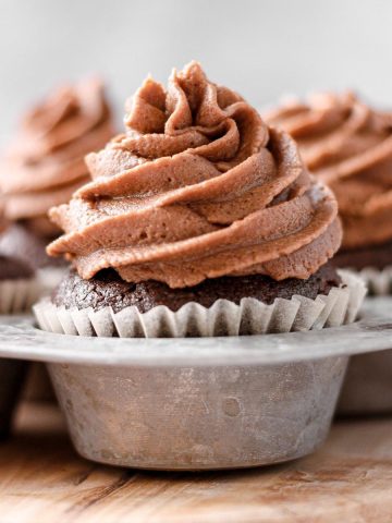 A chocolate cupcake with chocolate buttercream frosting in a metal cupcake tin.