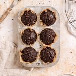 Six double chocolate banana muffins with mini chocolate chips in a muffin tin.