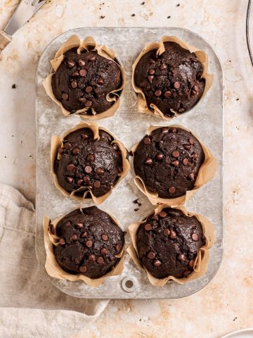 Six double chocolate banana muffins with mini chocolate chips in a muffin tin.
