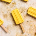 Homemade mango popsicles with wooden popsicle sticks.