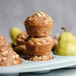 Healthy oatmeal pear muffins in a light blue muffin tin with whole Bartlett pears.