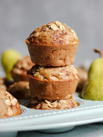 Healthy oatmeal pear muffins in a light blue muffin tin with whole Bartlett pears.