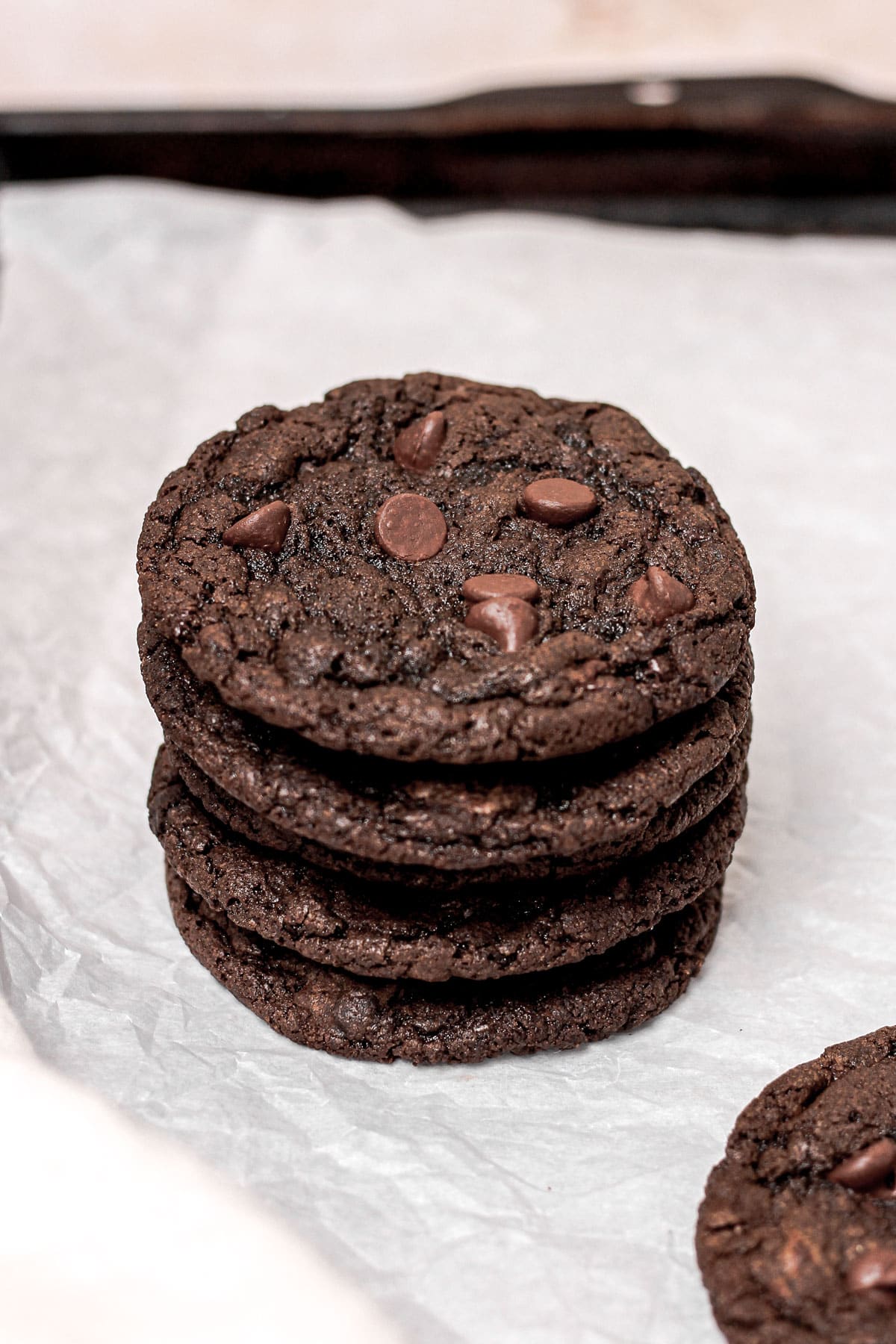 A stack of double chocolate chip cookies on a parchment lined baking sheet.