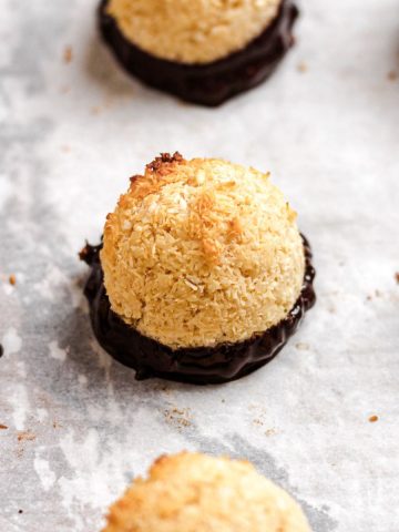 Coconut macaroons dipped in chocolate on parchment paper.