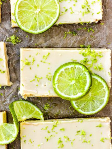 Key lime pie bars with fresh lime slices and lime zest on brown parchment paper.
