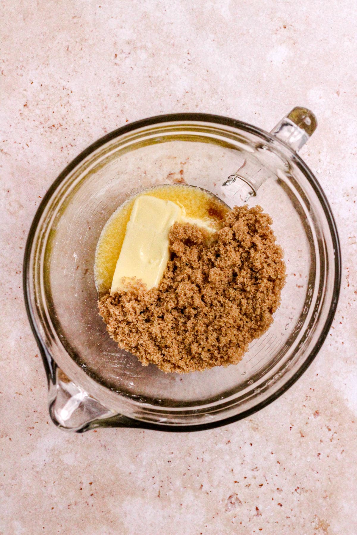 A glass bowl filled with softened butter and brown sugar for cookies.