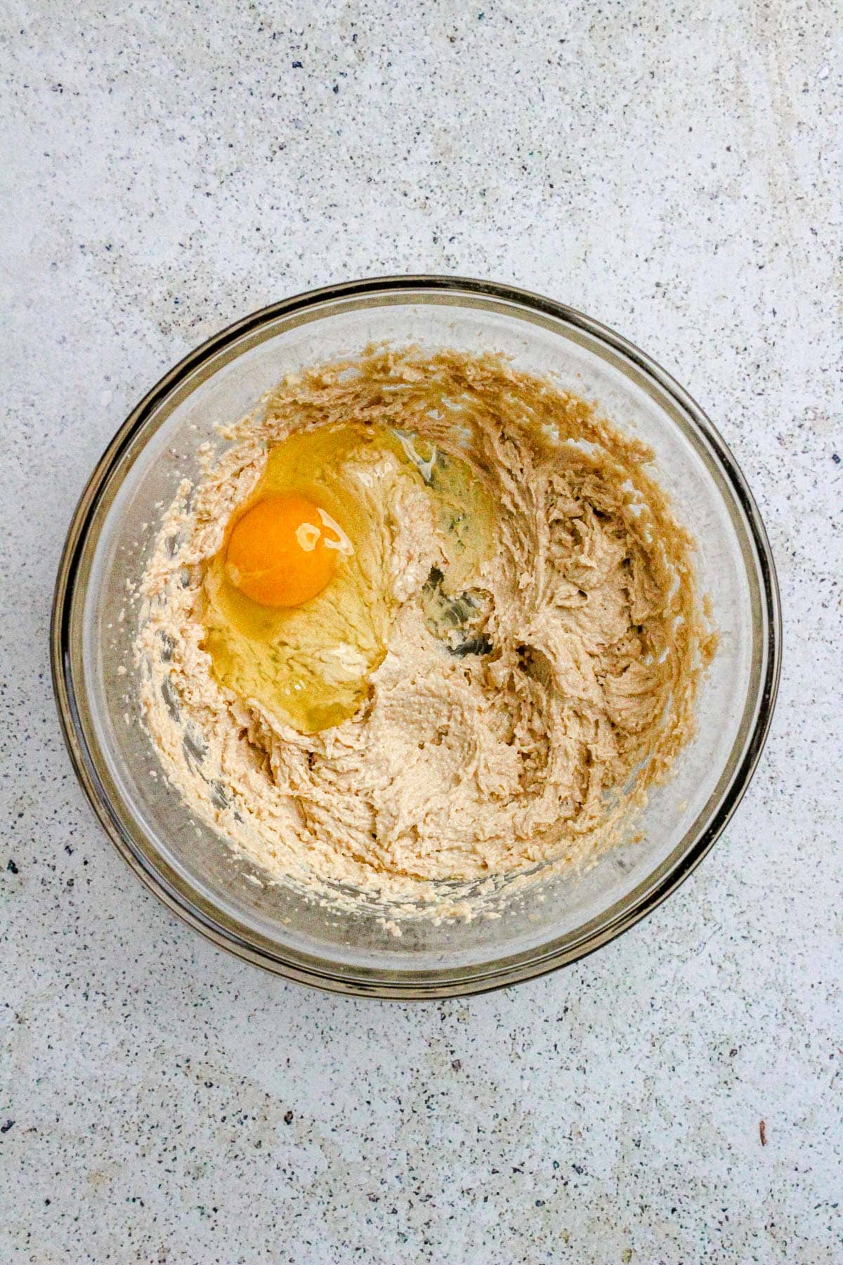 A glass bowl with creamed butter and sugar and an egg.
