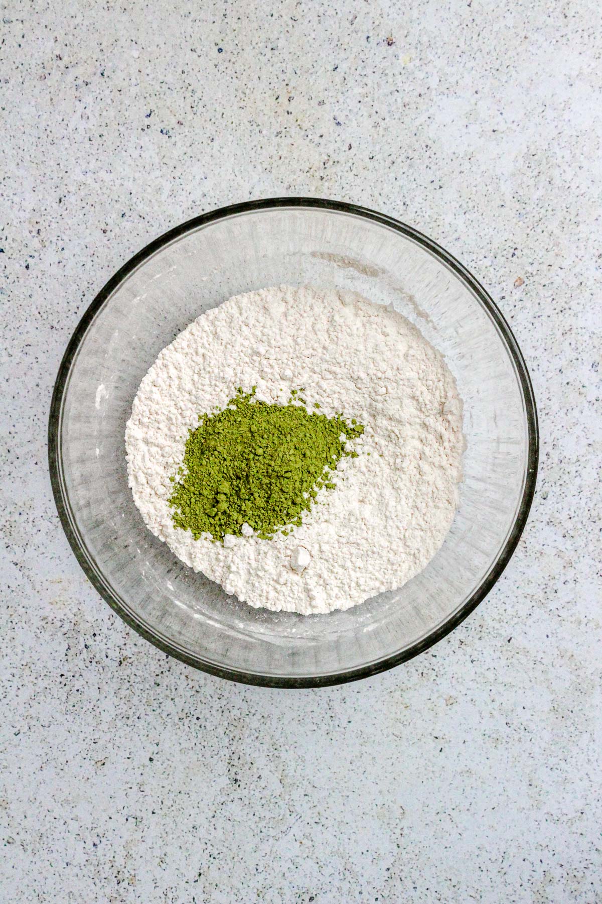 A glass bowl with flour and matcha powder for matcha cookies.