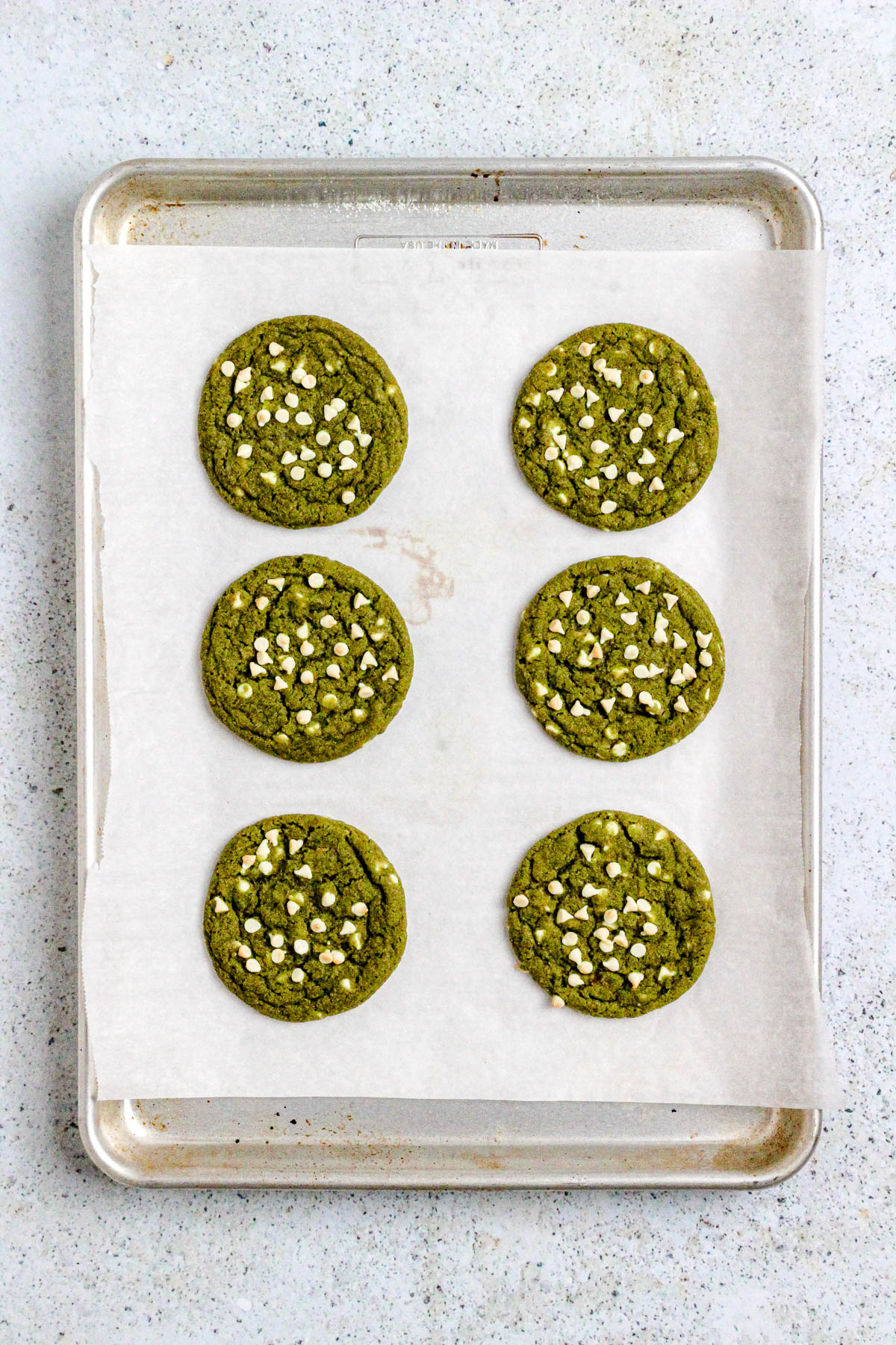 Matcha cookies with white chocolate chips on a parchment lined baking sheet.