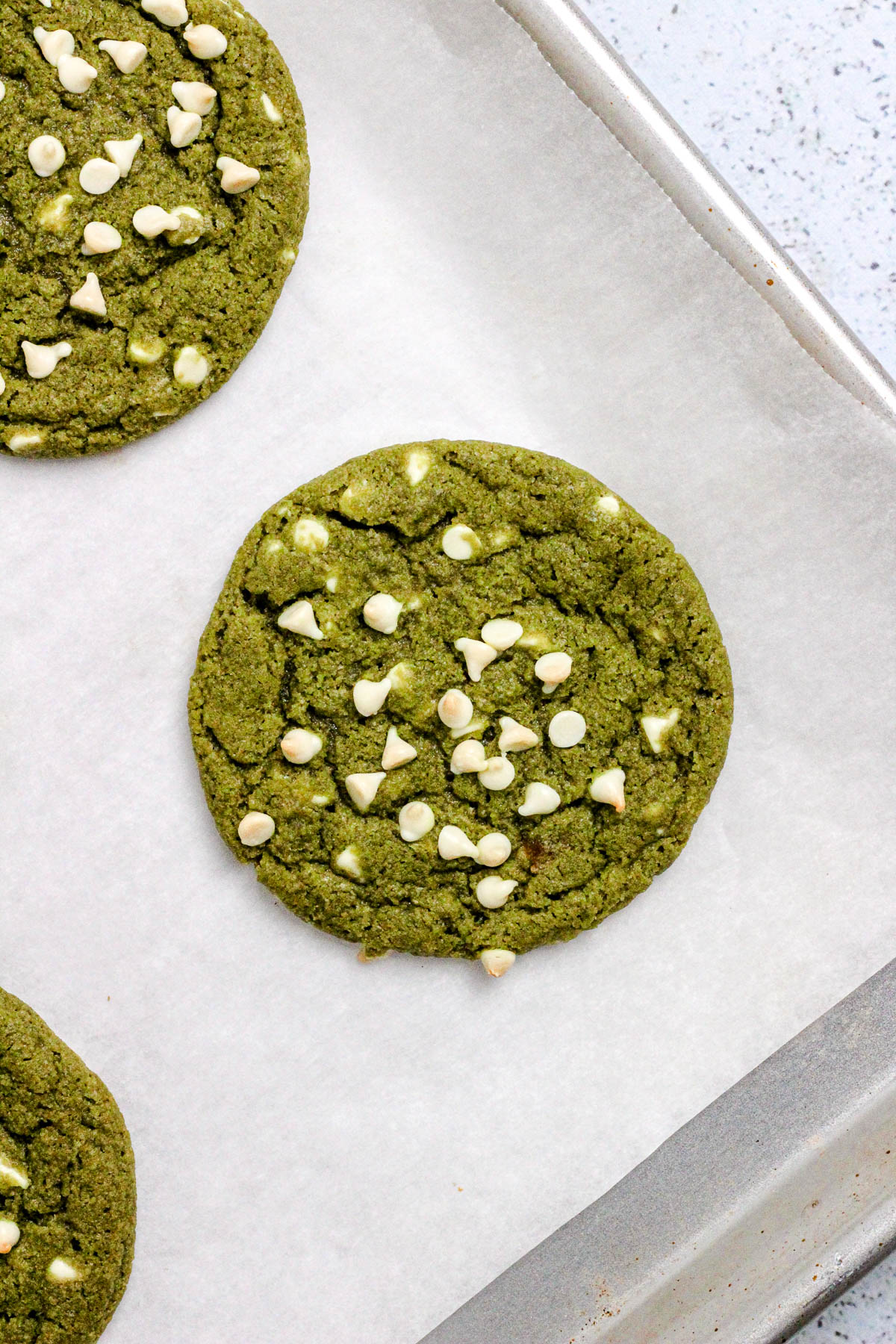 Matcha cookies with white chocolate chips on a parchment lined baking sheet.