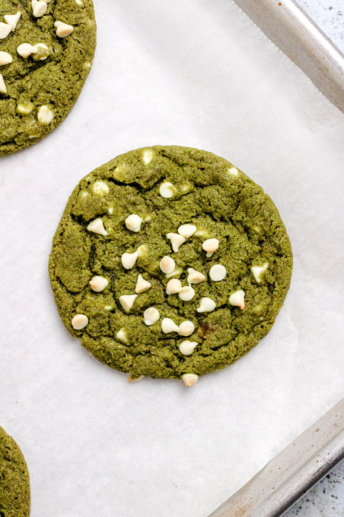 Matcha cookies with white chocolate chips on a parchment lined baking sheet.