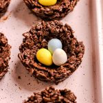 Birds nest cookies with mini chocolate eggs on a pink baking tray.
