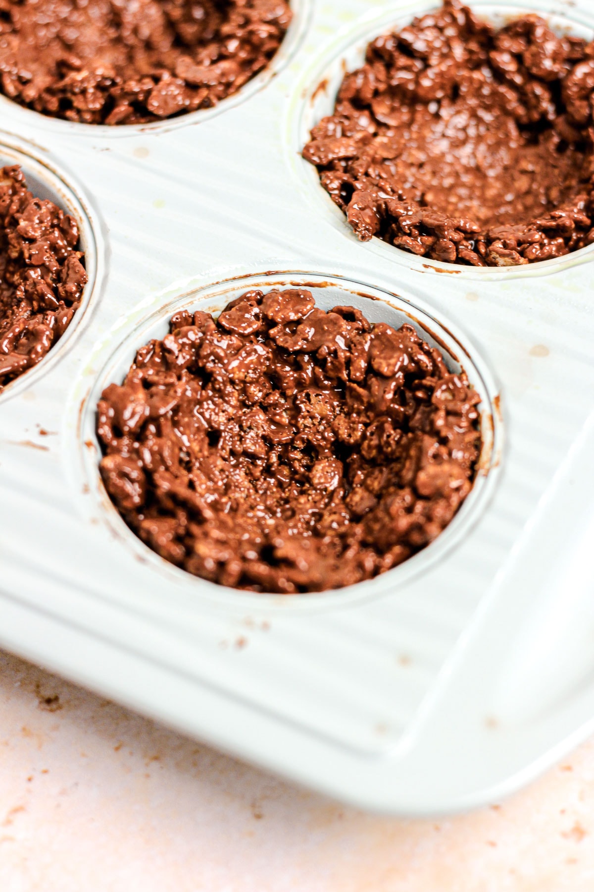 Chocolate peanut butter rice cereal mixture in a muffin tin for birds nest cookies.
