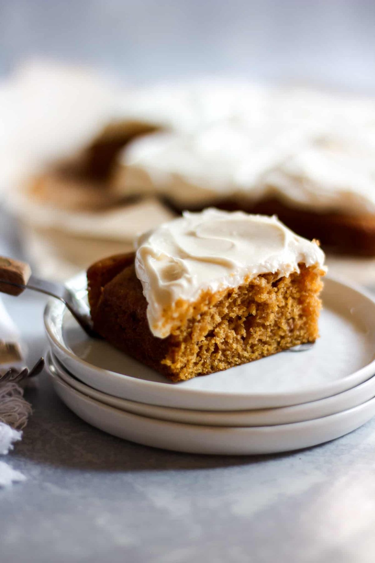 Best Pumpkin Cake with Cream Cheese Frosting a slice of pumpkin cake with white icing onto a stack of small white plates
