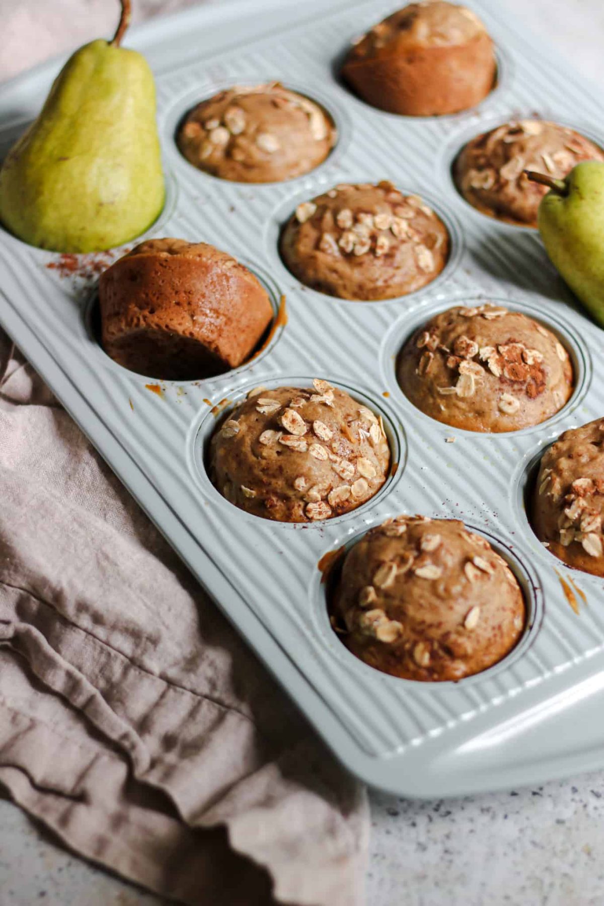 Cinnamon Pear Oat Muffins Flatlay of light blue muffin tin with pear muffins and linen kitchen towel