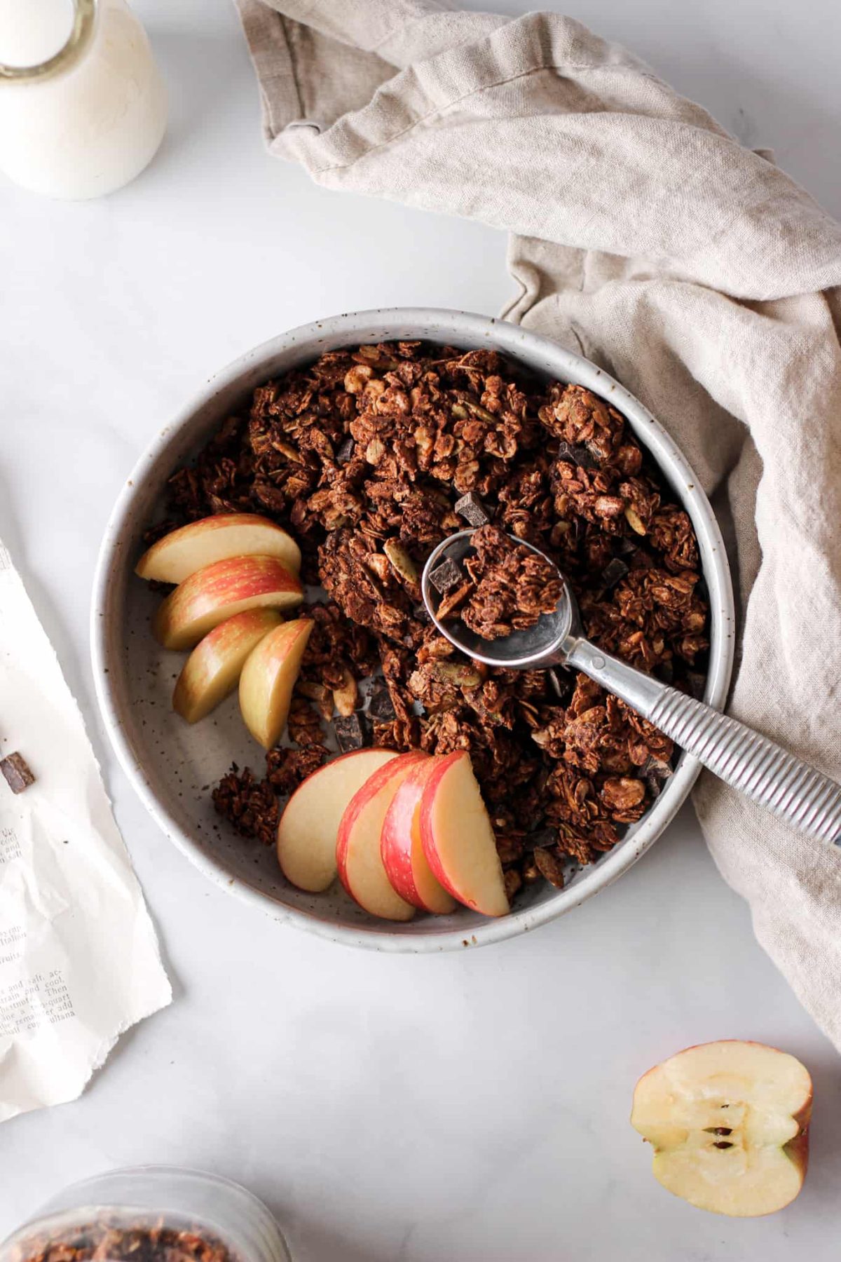 Dark Chocolate Granola a bowl of chocolate chunk granola with a spoon and sliced apples