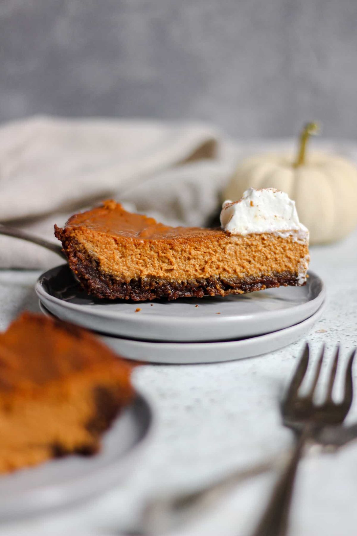 classic pumpkin pie with gingersnap crust side view of a slice of pumpkin pie with a dark cookie crust and whipped cream