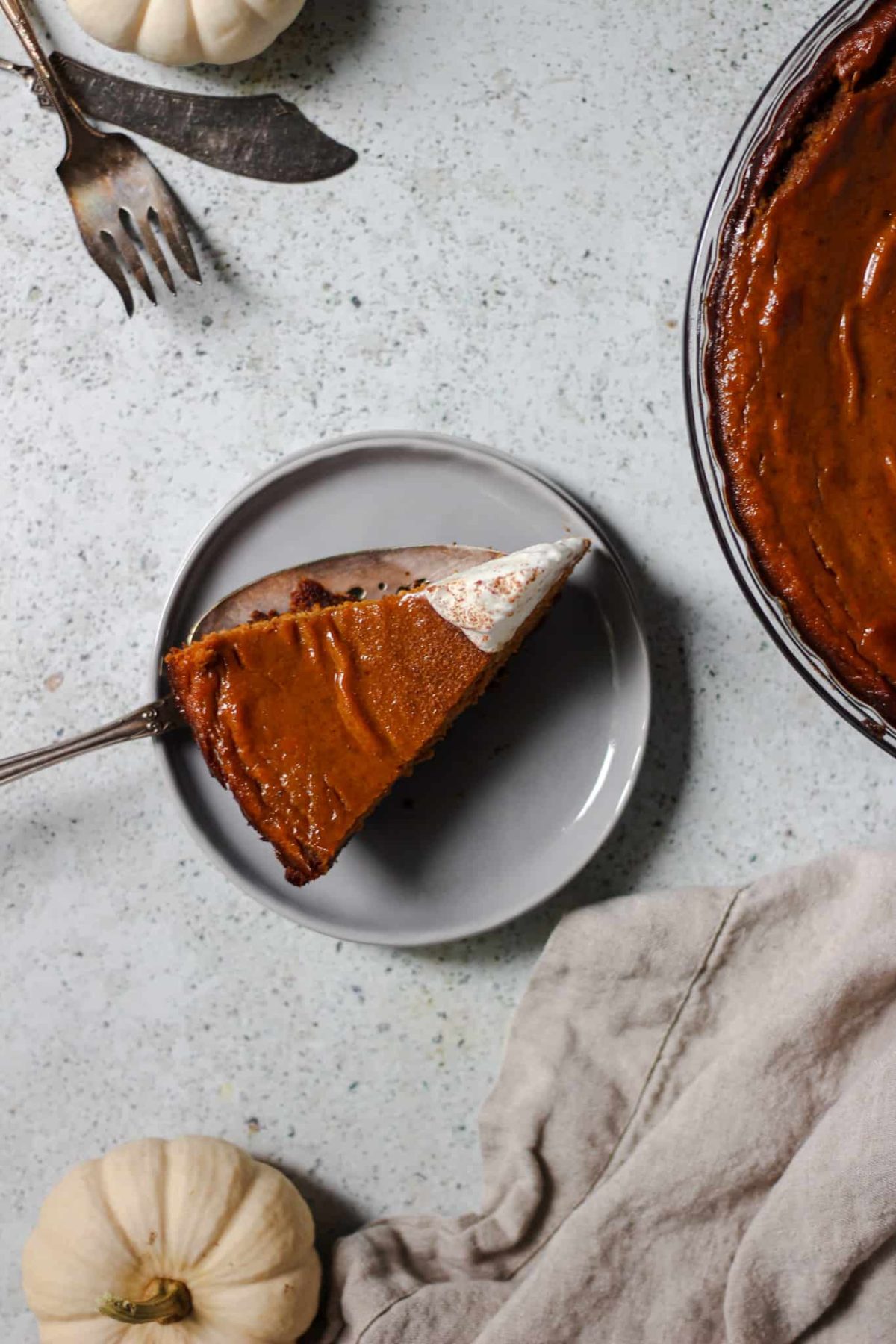 pumpkin pie with gingersnap cookie crust flatlay photo of a slice of fall pie with a linen, silverware and a small white pumpkin