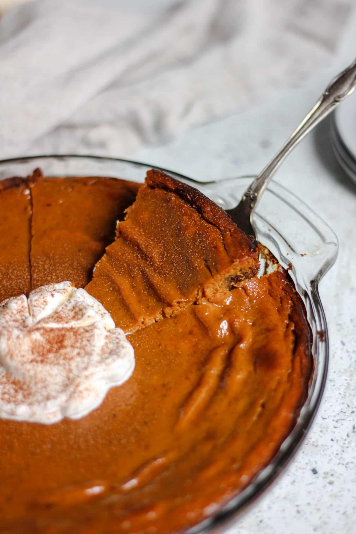 rich pumpkin pie with gingersnap crust serving a slice of pumpkin pie from a glass dish